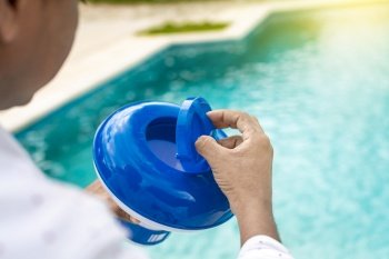 Hand of a pool disinfection worker holding a chlorine dispenser. Hands of a worker installing a pool chlorine float, a person holding a pool chlorine dispenser. Hands holding a pool chlorine dispenser.