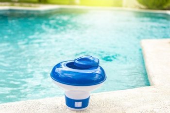 A chlorine dispenser for swimming pools with blue water in the background. Dosing float for swimming pool chlorination, A chlorine float on the edge of a swimming pool. 