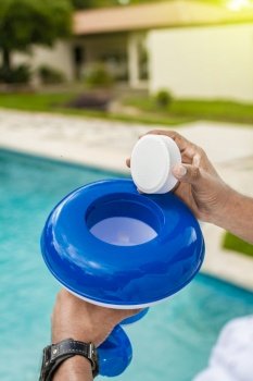 Hand of a pool disinfection worker holding a dispenser with a chlorine tablet. Hands holding a dispenser with pool chlorine tablet, pool float and chlorine tablets for pool maintenance. Hands holding a pool chlorine dispenser.