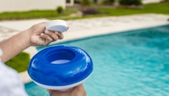 Hands holding a dispenser with pool chlorine tablet, pool float and chlorine tablets for pool maintenance. Hands holding a pool chlorine dispenser. Hand of a pool disinfection worker holding a dispenser with a chlorine tablet.
