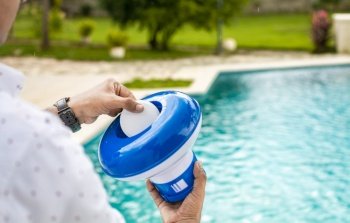 Pool float and chlorine tablets for pool maintenance. Hands holding a pool chlorine dispenser. Hand of a pool disinfection worker holding a dispenser with a chlorine tablet. Hands holding a dispenser with pool chlorine tablet
