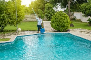 Man cleaning a swimming pool with skimmer, maintenance person cleaning a swimming pool with skimmer, swimming pool cleaning and maintenance concept.