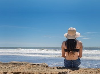 woman in hat from back to the sea, girl in hat looking to the sea, vacation concept, rear view of a girl watching the sea