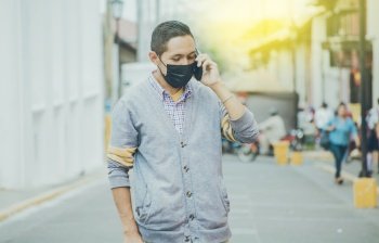 Man with surgical mask calling on the phone, latin man with mask calling on the phone in the street, man in mask calling on the phone in the street