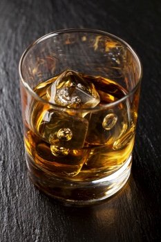 Glass of scotch whiskey with ice on black stone table