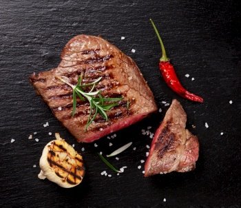 Grilled beef steak with rosemary, salt and pepper on black stone plate. Top view