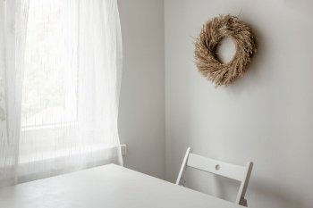Floral dried wreath hanging on white wall in a light room. Minimal composition. Neutrals. Floral dried wreath hanging on white wall in a room