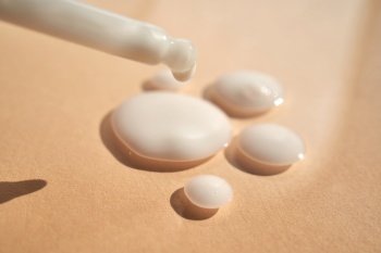 Drops of white cosmetics on a beige background with a dropper.. Drops of white cosmetics on a beige background.