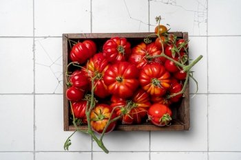 Box of mix red tomatoes in summer day. Composition of variety fresh tomatoes. White tile background. Top view.. Mix red tomatoes