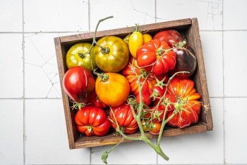 Box of mix colorful tomatoes in summer day. Composition of variety fresh tomatoes. White tile background. Top view.. Mix colorful tomatoes
