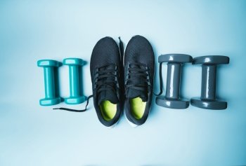 Workout flat-lay with sneakers and dumbbell on blue background top view. Sport and fitness concept. Workout flat-lay with sneakers