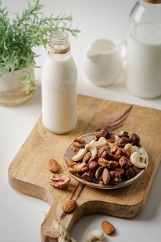 Vegan milk from nuts in glass jar with various nuts on white stone background. Vegan milk from nuts