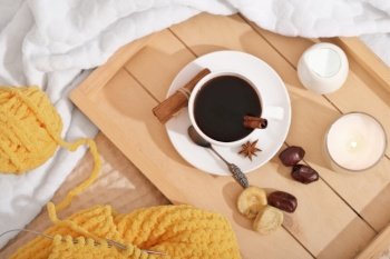 cinnamon coffee in a white cup, dry fruits, milk and candle in a wooden tray. knitted yellow scarf and yarn ball on a bed with soft plaid. cozy winter morning. . cinnamon coffee in a white cup, dry fruits, milk and candle in a wooden tray. knitted yellow scarf and yarn ball on a bed with soft plaid. cozy winter morning 