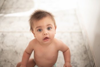 Blue-eyed baby sitting on the floor at home