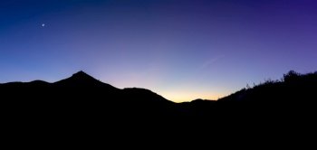 A panorama landscape of mountains and crags in silhouette under a nighttime sky with the fading glow of sunset