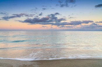 View of calm turquoise ocean water under a olorful sunset sky with calm waves on the sandy shore