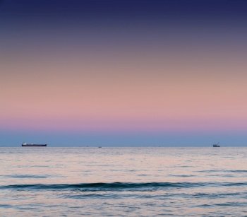 Colorful sunset on the Black Sea off the Bulgarian coast with a fishing boat and a freight ship on the horizon