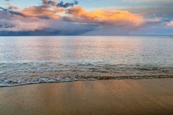 Background of gentle waves on golden sand beach with ocean and colorful sunset sky behind