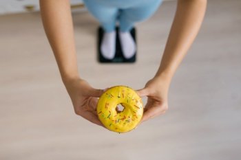 Sweet donut in the hands of a woman standing on the scales