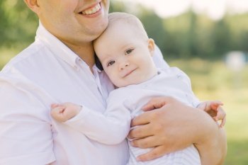 A young father of a large size holds his little son in his arms in the park in the summer
