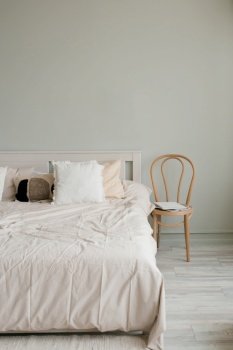 Bedroom interior in Scandinavian style. A bed with beige linens and pillows and a chair by the bed