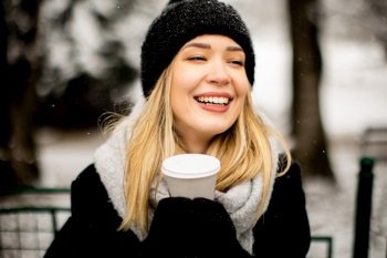 Pretty young woman n warm clothes enjoying in snow with takeaway coffee cup