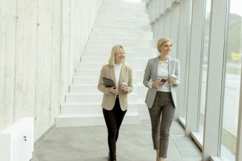 Two business women walking with digital tablet and mobile phone in the office corridor