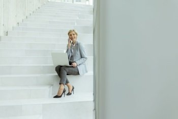 Businesswoman using mobile phone while working on laptop on the modern office stairs