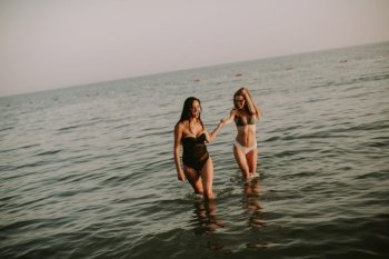 Two pretty young women having fun on the beach by the sea at sunset