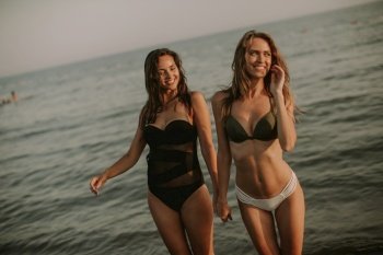 Two pretty young women having fun on the beach by the sea at sunset