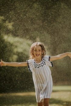 Cute little girl having fun with water under irrigation sprinkler