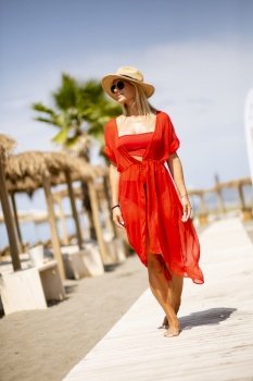 Pretty young woman in red dress walking on a beach at summer