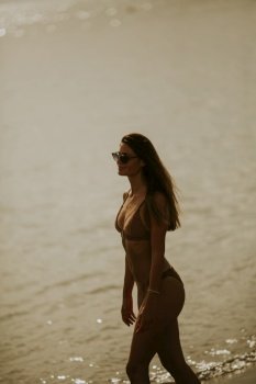 Pretty young woman in bikini walking by the sea on a sunset of summer day