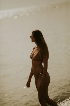 Pretty young woman in bikini walking by the sea on a sunset of summer day