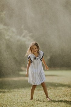 Cute little girl having fun with water under irrigation sprinkler