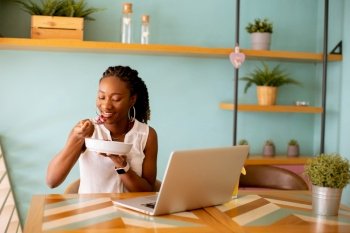 Pretty young black woman having a healthy breakfast while working on laptop in the cafe