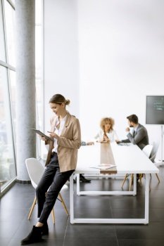 Young woman holding digital tablet and working in modern office in front of her team