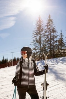 Young woman enjoying winter day of skiing on the snow covered slopes, surrounded by tall trees and dressed for cold temperatures