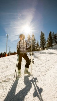 A single young female enjoys a sunny winter day of skiing, dressed in full snow gear with ski boots and sunglasses.