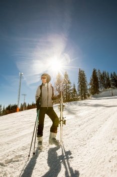 A single young female enjoys a sunny winter day of skiing, dressed in full snow gear with ski boots and sunglasses.