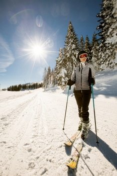 A single young female enjoys a sunny winter day of skiing, dressed in full snow gear with ski boots and sunglasses