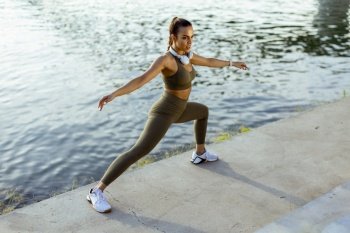 Pretty young woman in sportswear stretching on a river promenade