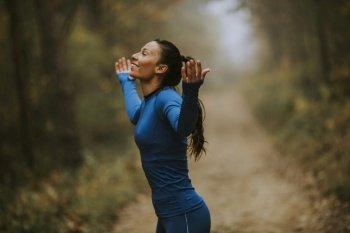 Pretty young woman in blue track suit spreading arms and taking deep breath in a forest