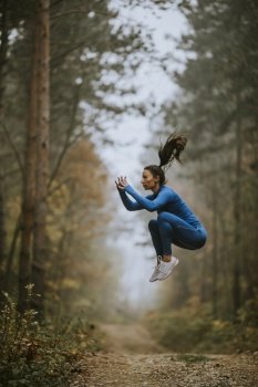 Young woman in blue track suit taking high jump on the forest trail at autumn