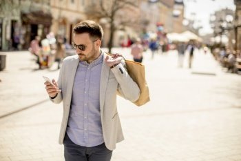 Portrait of cheerful handsome man goes  shopping in the city while uses mobile phone