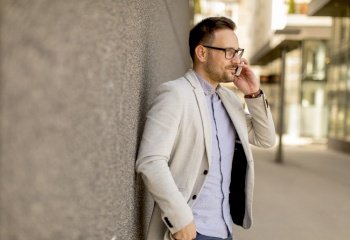 Handsome young businessman with mobile phone by the grey wall