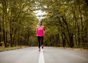 Young fitness woman running at forest trail in golden autumn