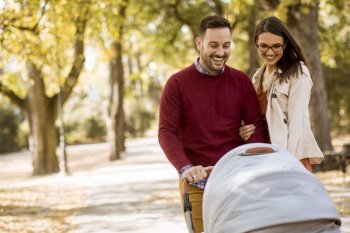 Happy young parents walking in the autumn park and driving a baby in baby carriage