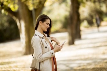 Side view at young woman using mobile phone in autumn park