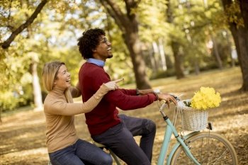 Multiracial young couple riding on a bicycle at the autumn park